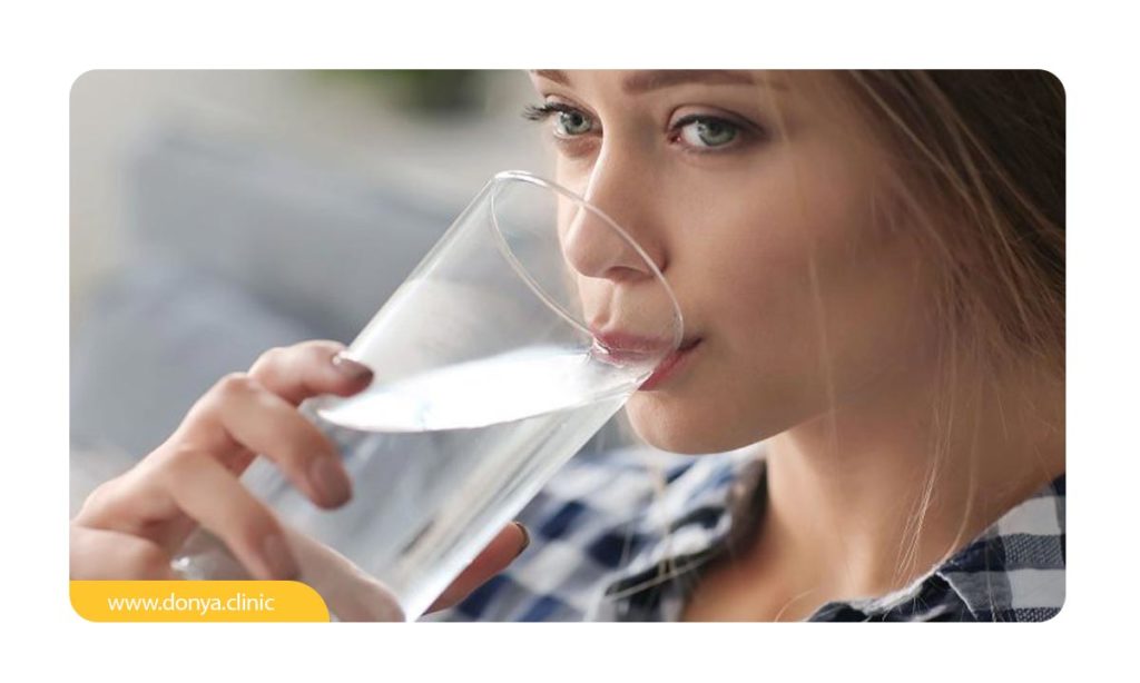 خانمی که در حال نوشیدن آب از یک لیوان بزرگ جهت رفع تلخی دهان است